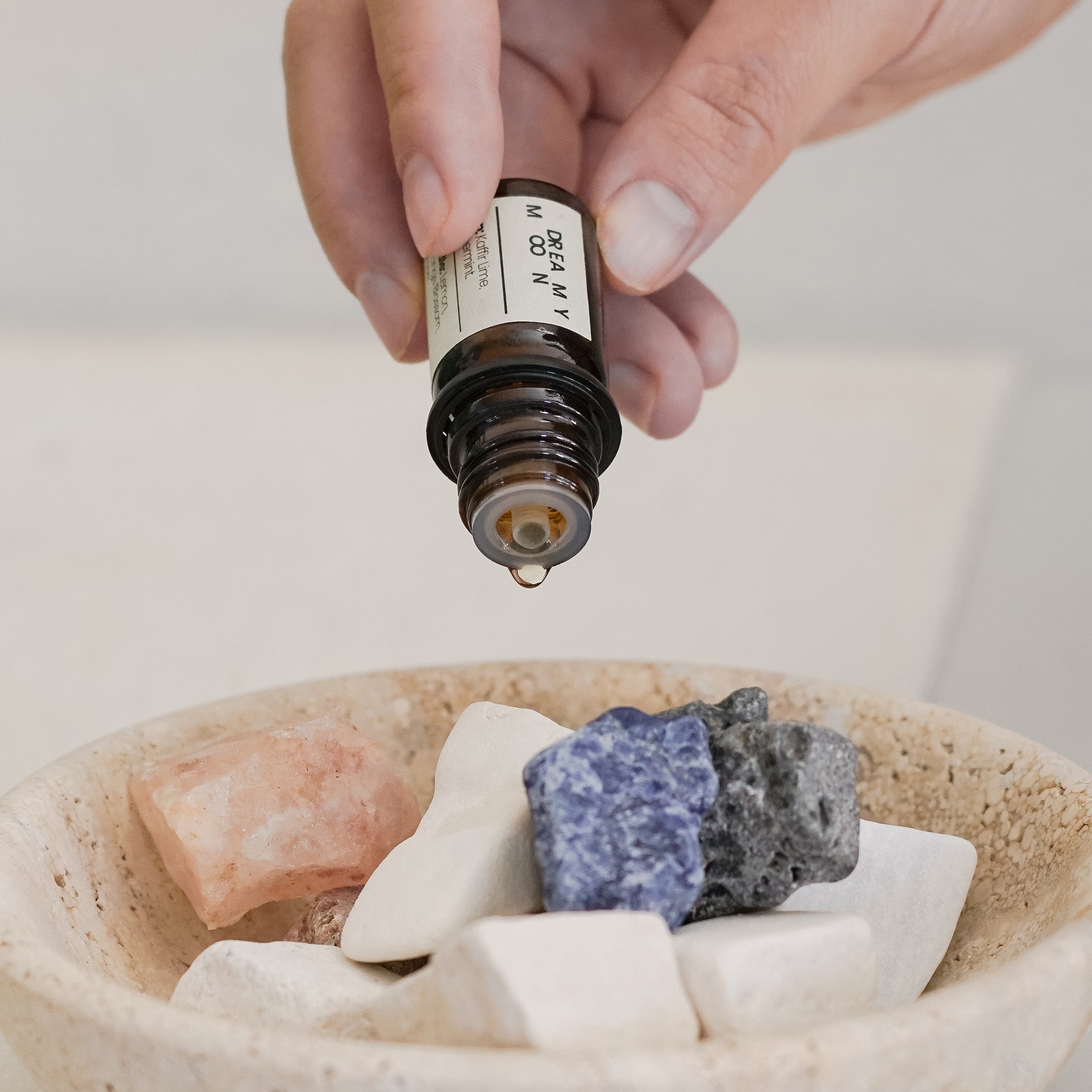 Hand holding a dropper over stones in a bowl with a neutral background