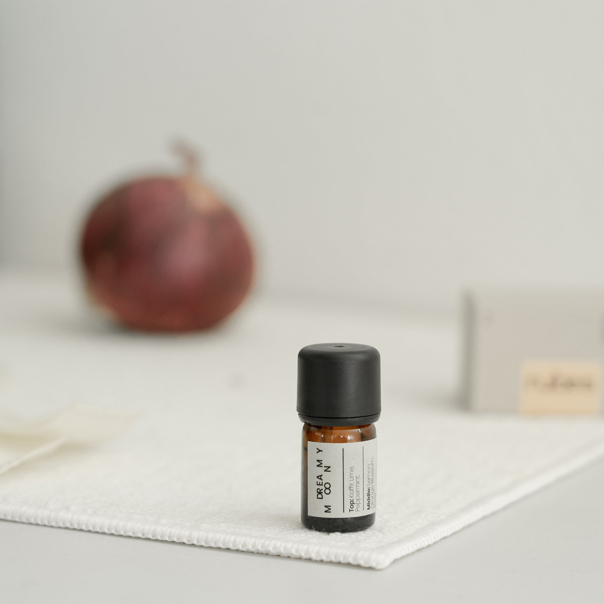 Small essential oil bottle with a black cap on a white surface, with a blurred onion in the background.