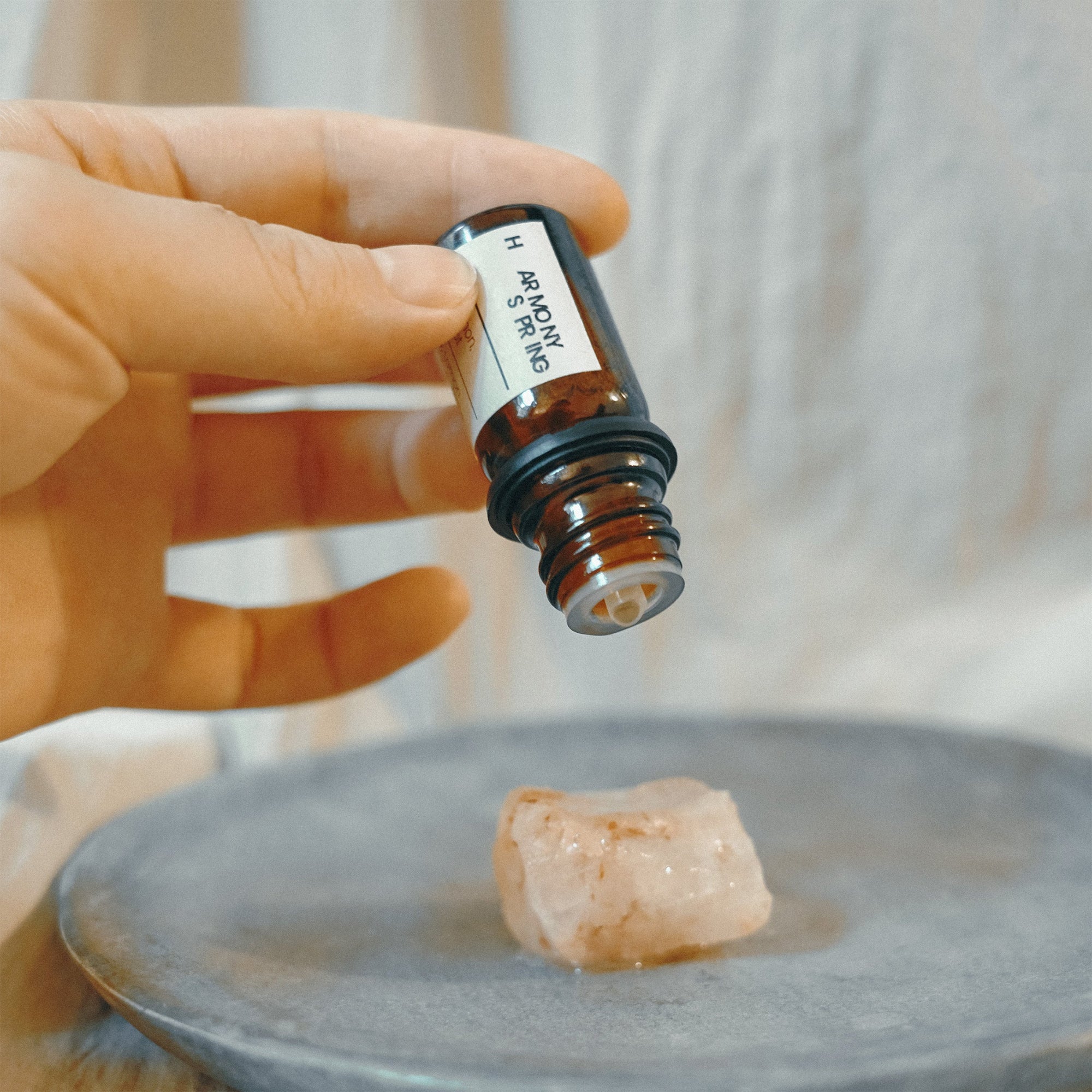 Hand holding an essential oil bottle above a piece of stone on a gray plate.
