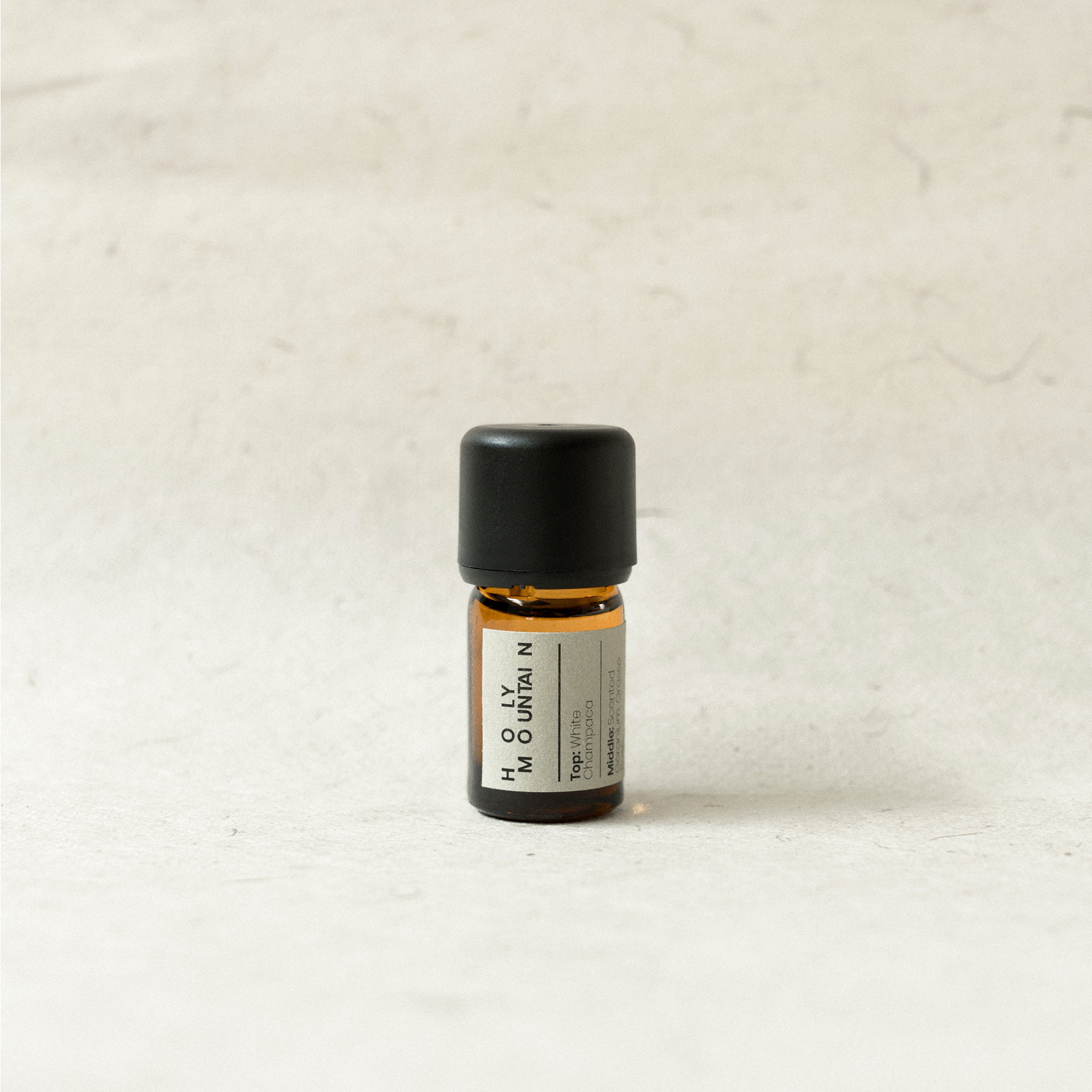 Small essential oil bottle with black cap on a light beige background