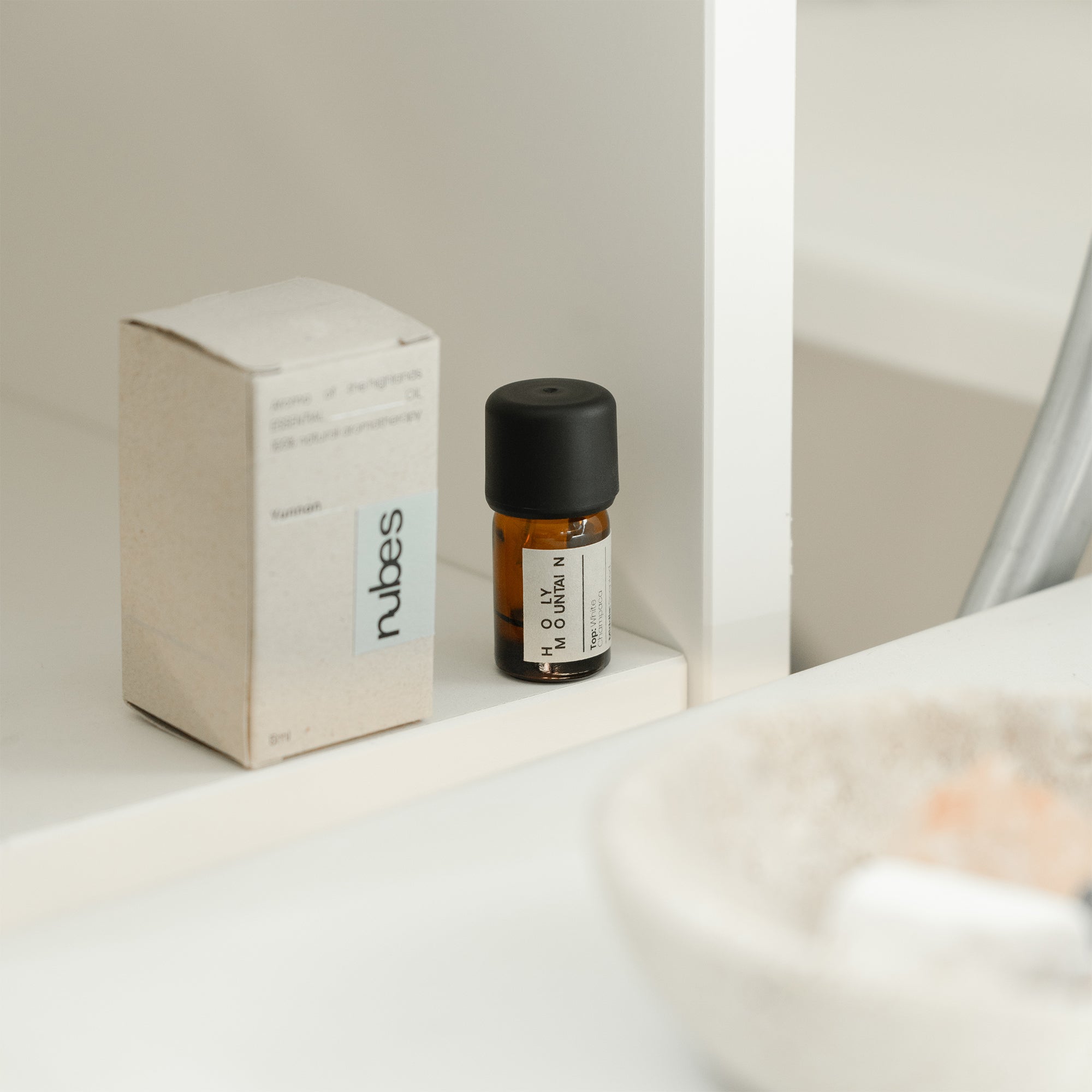 Small bottle with black cap and white label on a white surface next to a cardboard box with &