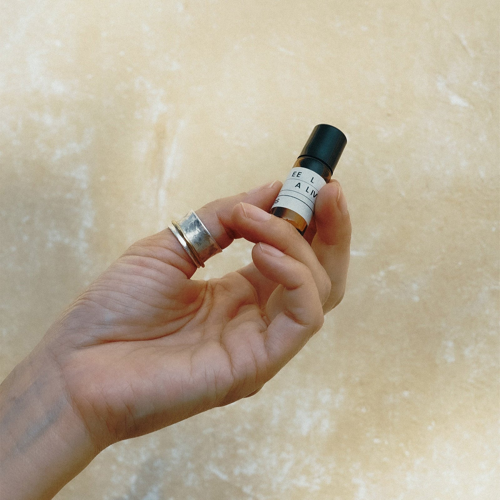 Hand holding a small bottle of perfume against a beige background