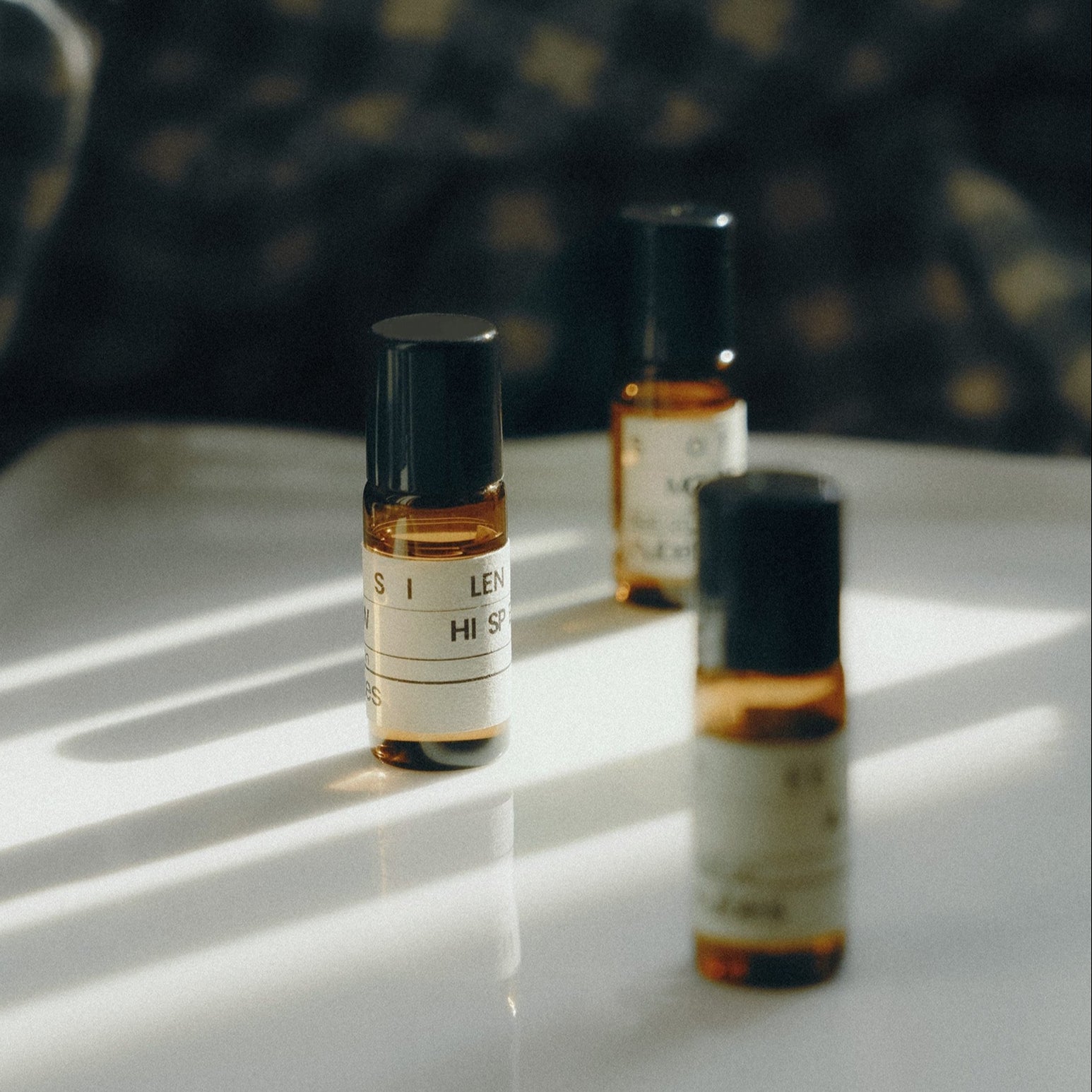 Three small glass bottles with labels on a reflective surface with a blurred background