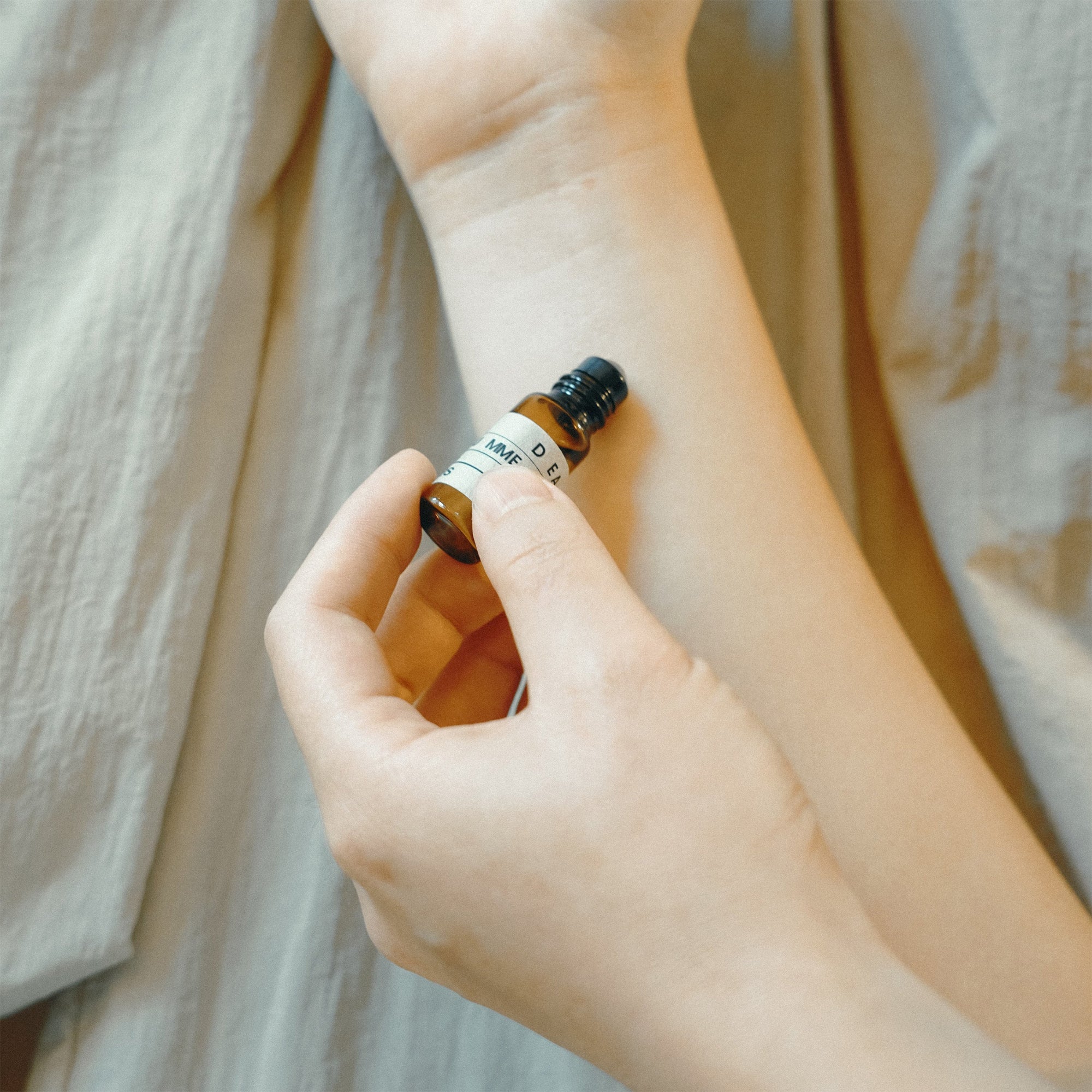 Hand holding a small brown bottle with a white label against a neutral background