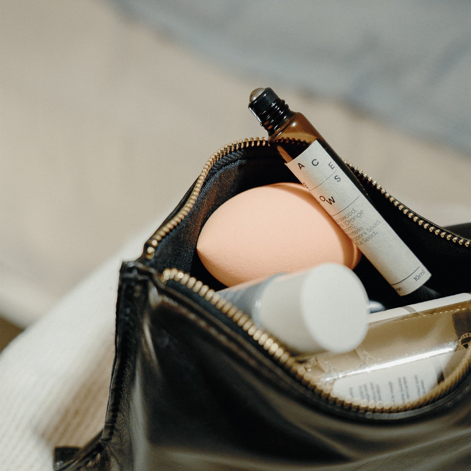 Open black makeup bag with skincare products on a light background