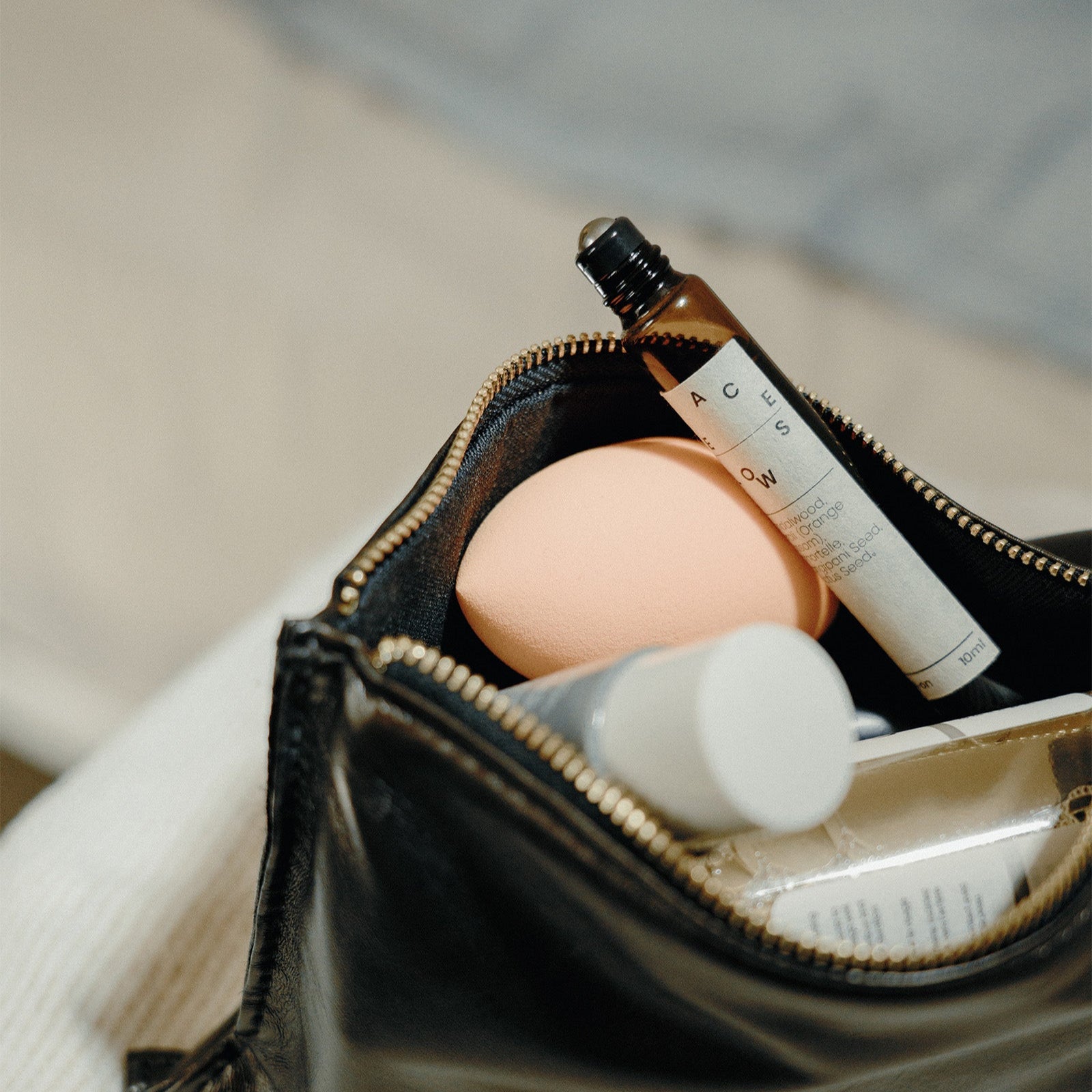 Open black makeup bag with skincare products on a light background