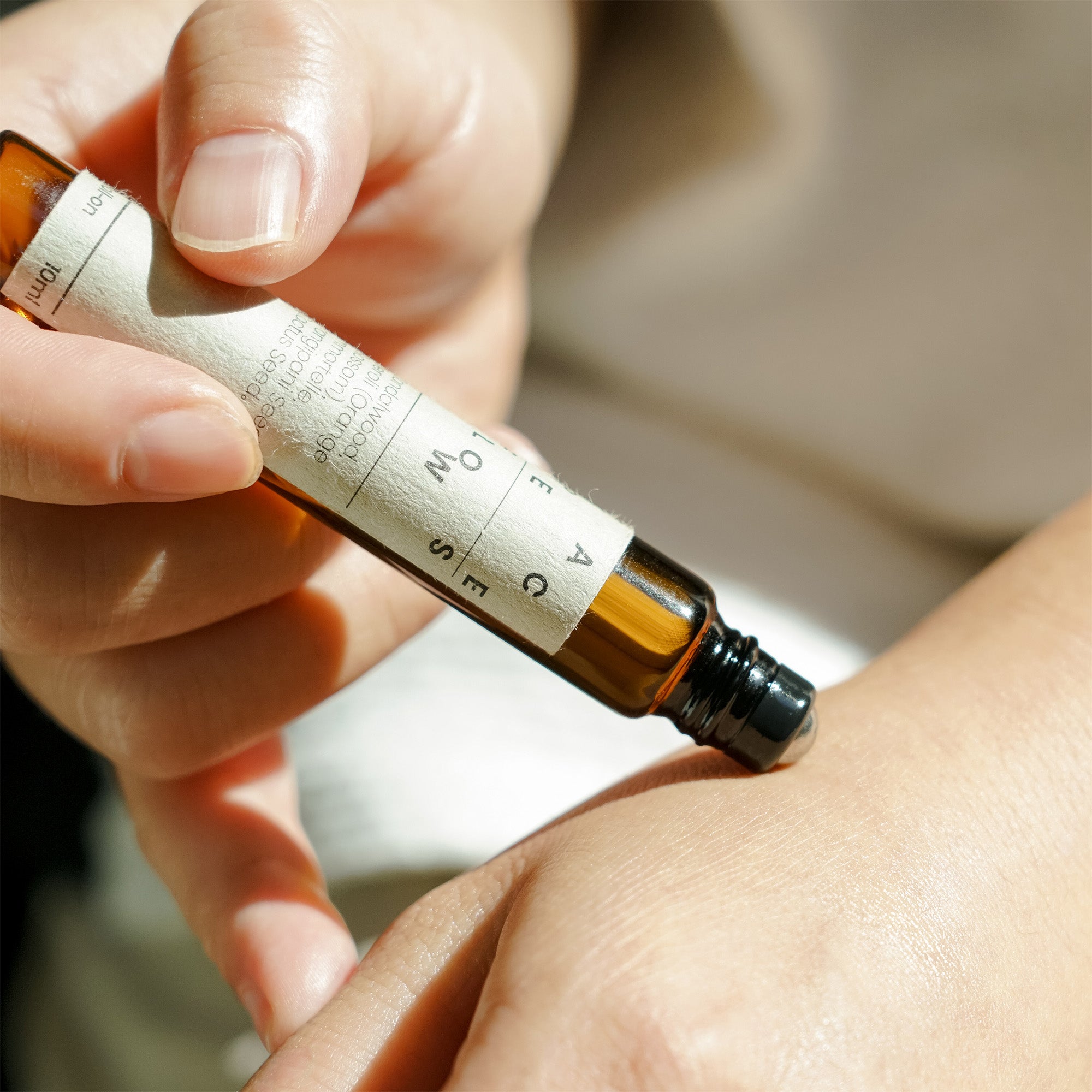 Hand holding a small brown bottle with a label, applying it to skin.