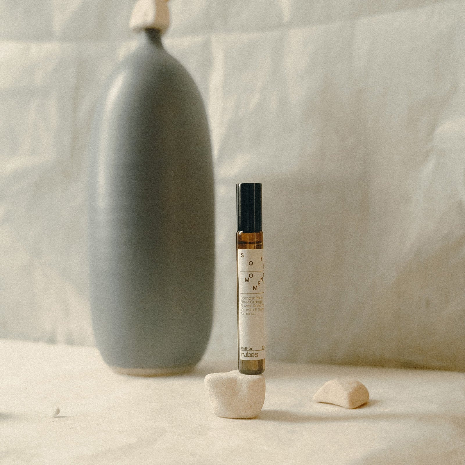 Small bottle with a label on a textured surface next to a ceramic vase