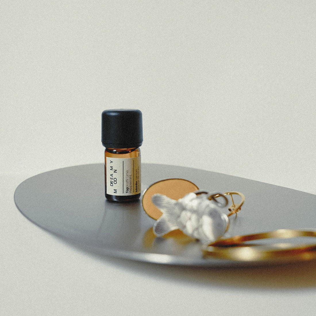 Small bottle of essential oil on a metallic tray with jewelry on a light background