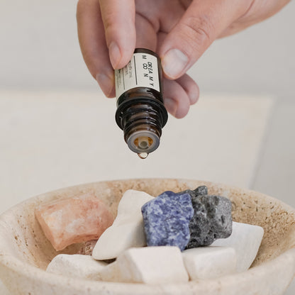 Hand holding a dropper over stones in a bowl with a neutral background