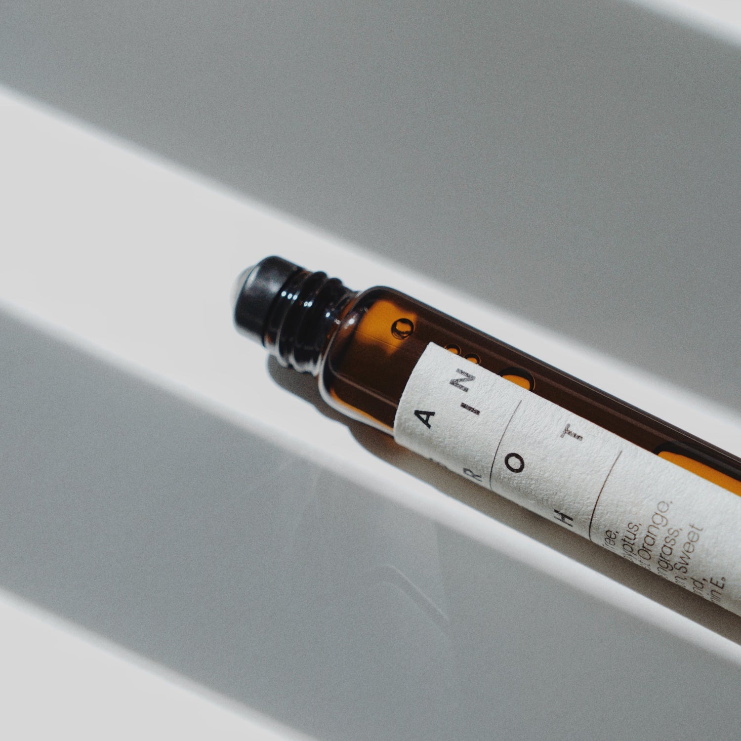 Nubes Brain Shot essential oil roll-on bottle lying diagonally in striped sunlight, highlighting its amber glass and minimalist label.