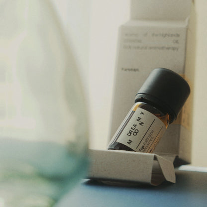 A soft, tranquil photograph featuring a Nubes Dreamy Moony Essential Oil bottle resting on its eco-friendly packaging. With warm amber glass and a minimalist label, the scene is bathed in gentle light, evoking relaxation and mindfulness.