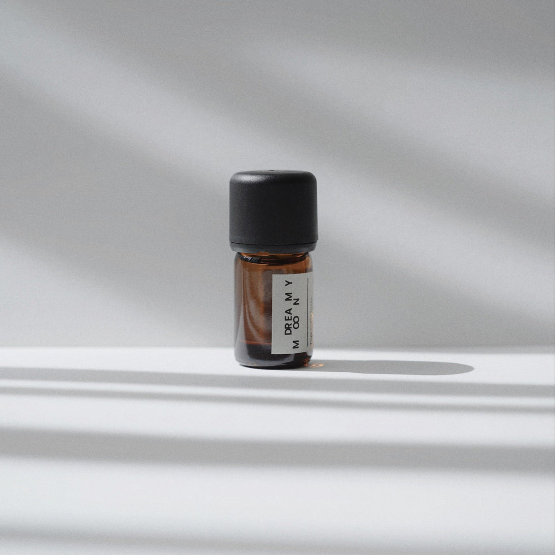 A Nubes Dreamy Moon Essential Oil Roll-On bottle stands in soft, striped light, casting gentle shadows for a minimalist and tranquil composition.