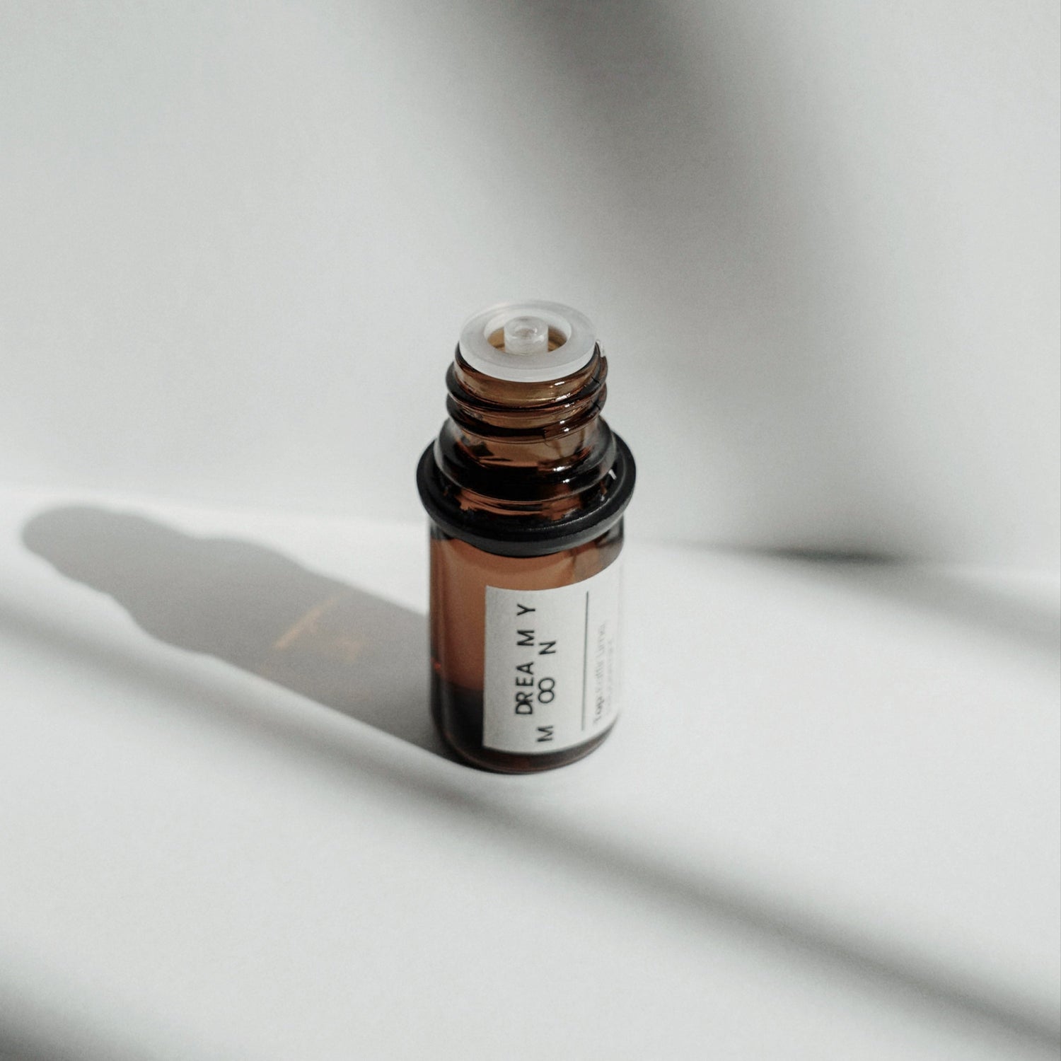 An open Nubes Dreamy Moon Essential Oil Roll-On bottle in soft, striped light, casting gentle shadows for a minimalist and calming composition.