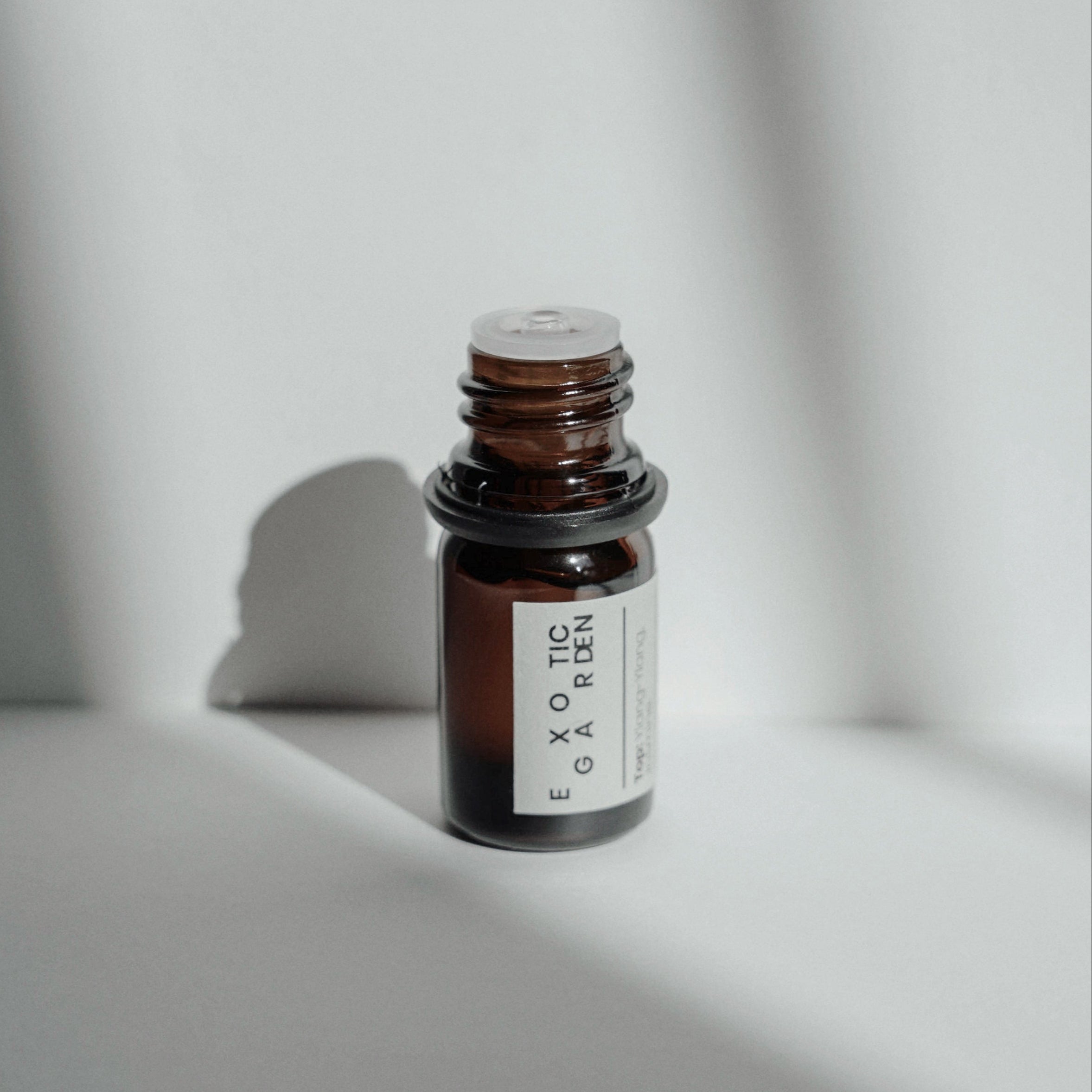 Nubes Exotic Garden essential oil bottle with an open top, bathed in soft natural light and shadows.