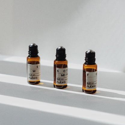 Three Nubes Essential Oil Roll-Ons stand in soft, striped sunlight, their amber glass glowing against a clean, minimalist background.