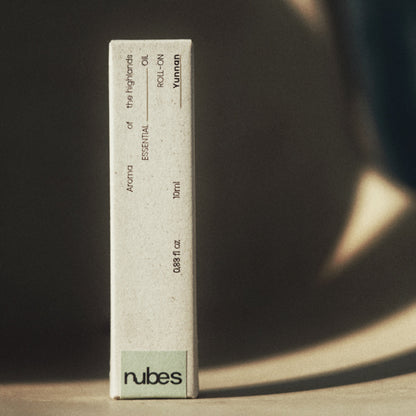 Nubes essential oil roll-on packaging standing upright in warm, directional light, casting dramatic shadows on a neutral surface.