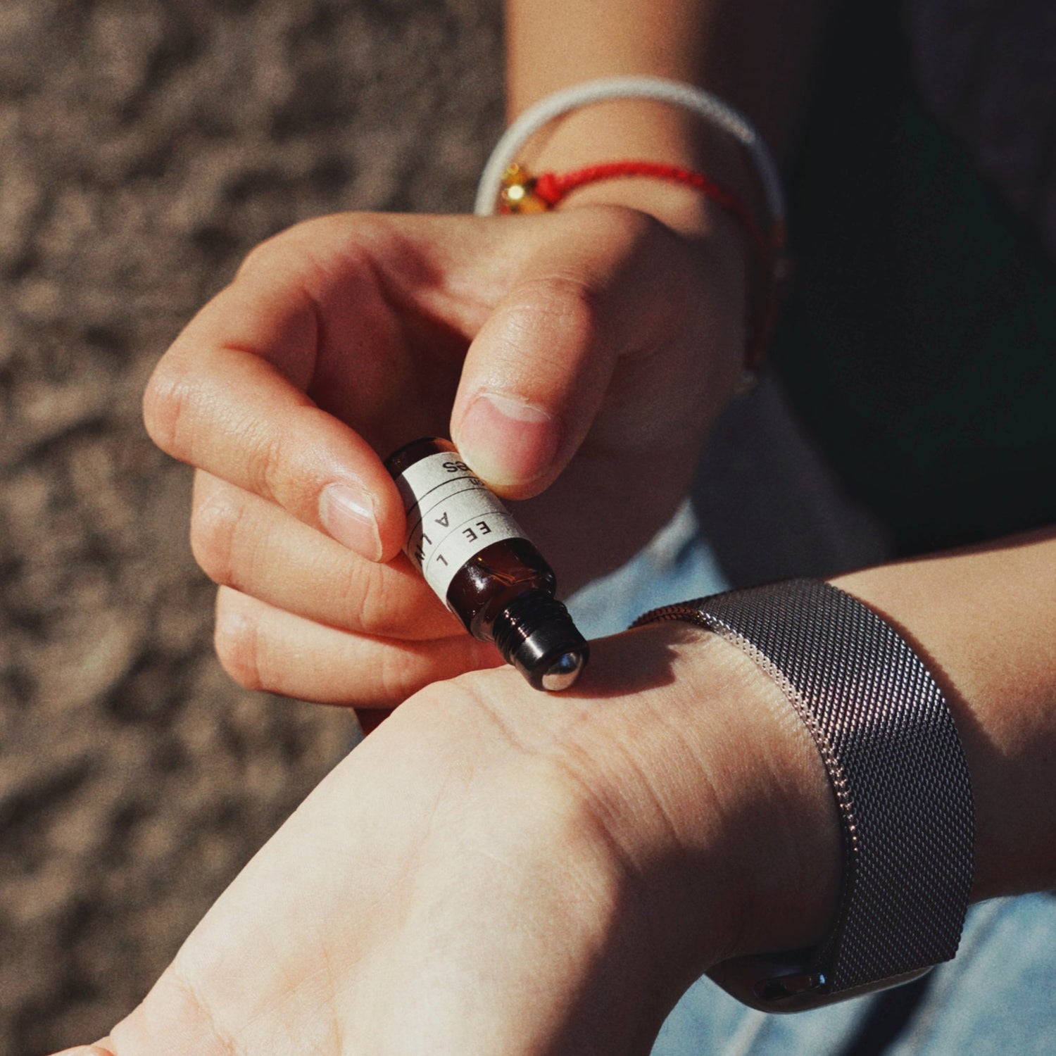 Hand applying Nubes roll-on essential oil blend to wrist outdoors, 3ml glass bottle with minimalist label &quot;Feel Alive&quot;, natural daylight photo