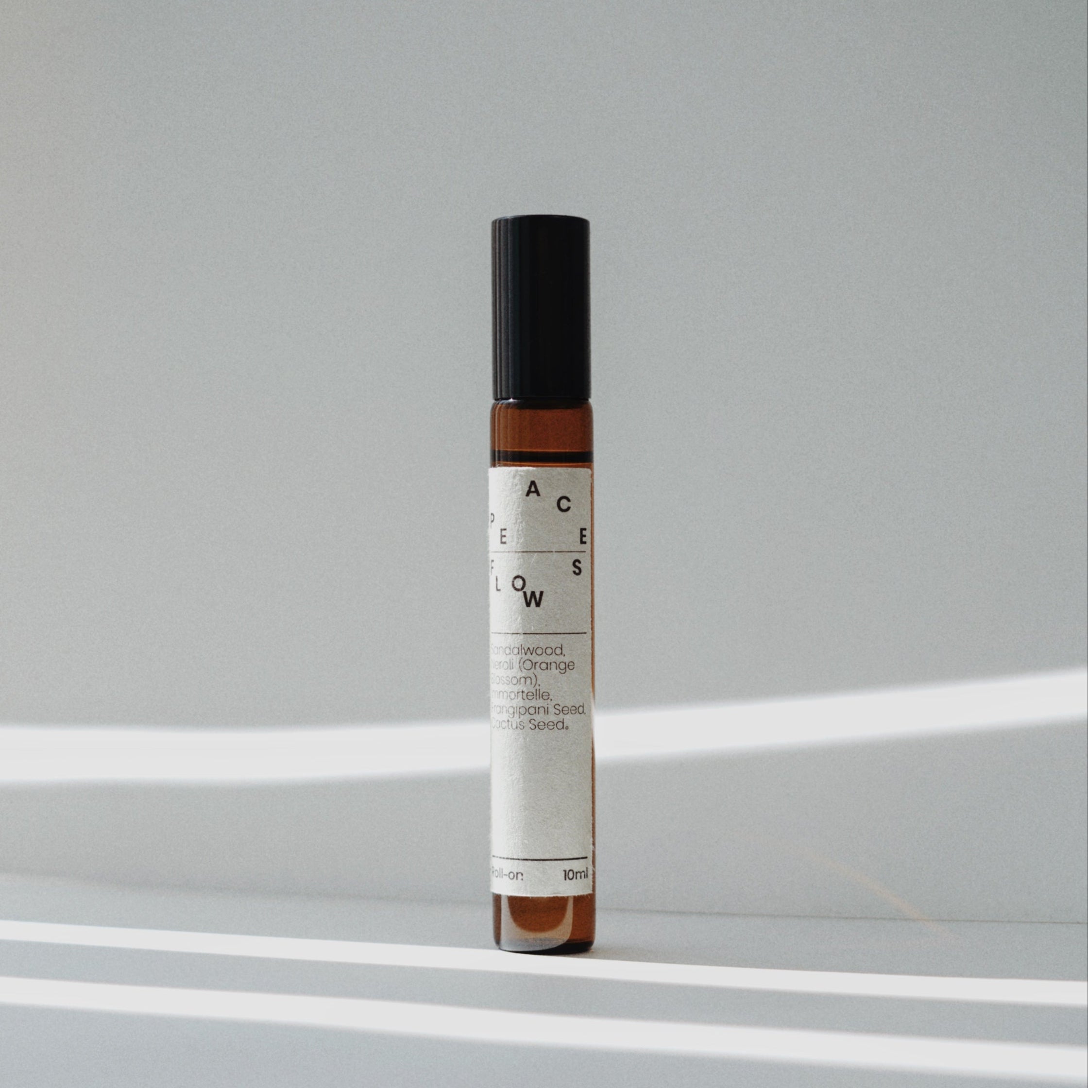 Nubes roll-on essential oil &quot;Peace Flows&quot; standing in soft natural light with striped shadows.