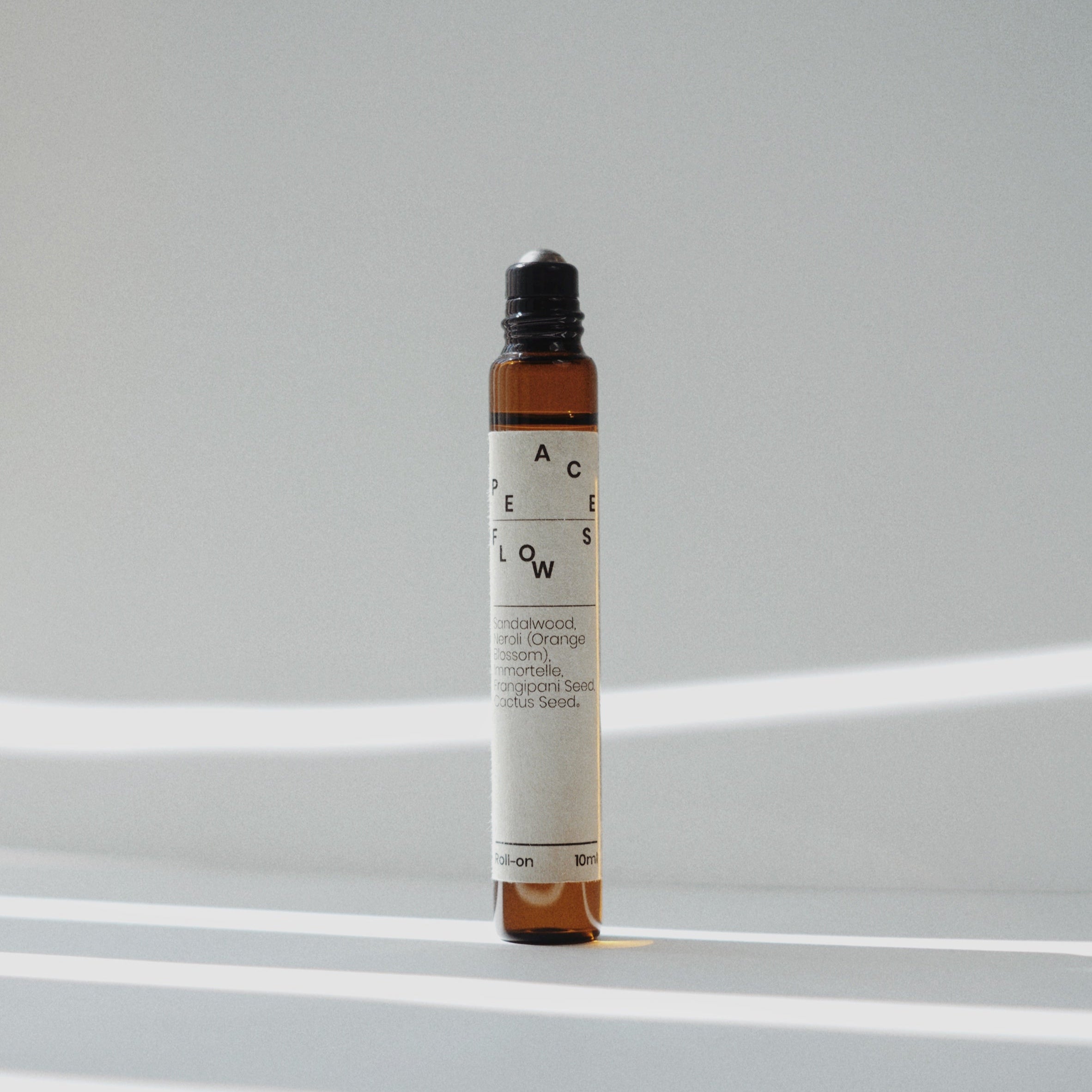 Nubes roll-on essential oil &quot;Peace Flows&quot; with an open applicator, bathed in soft striped light.
