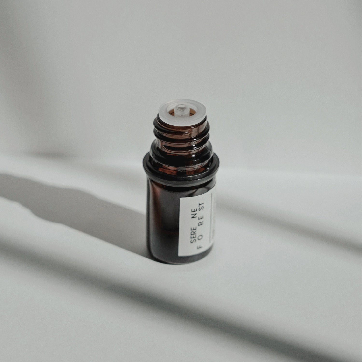 Nubes Serene Forest Essential Oil bottle with cap removed, bathed in soft shadows and natural light.