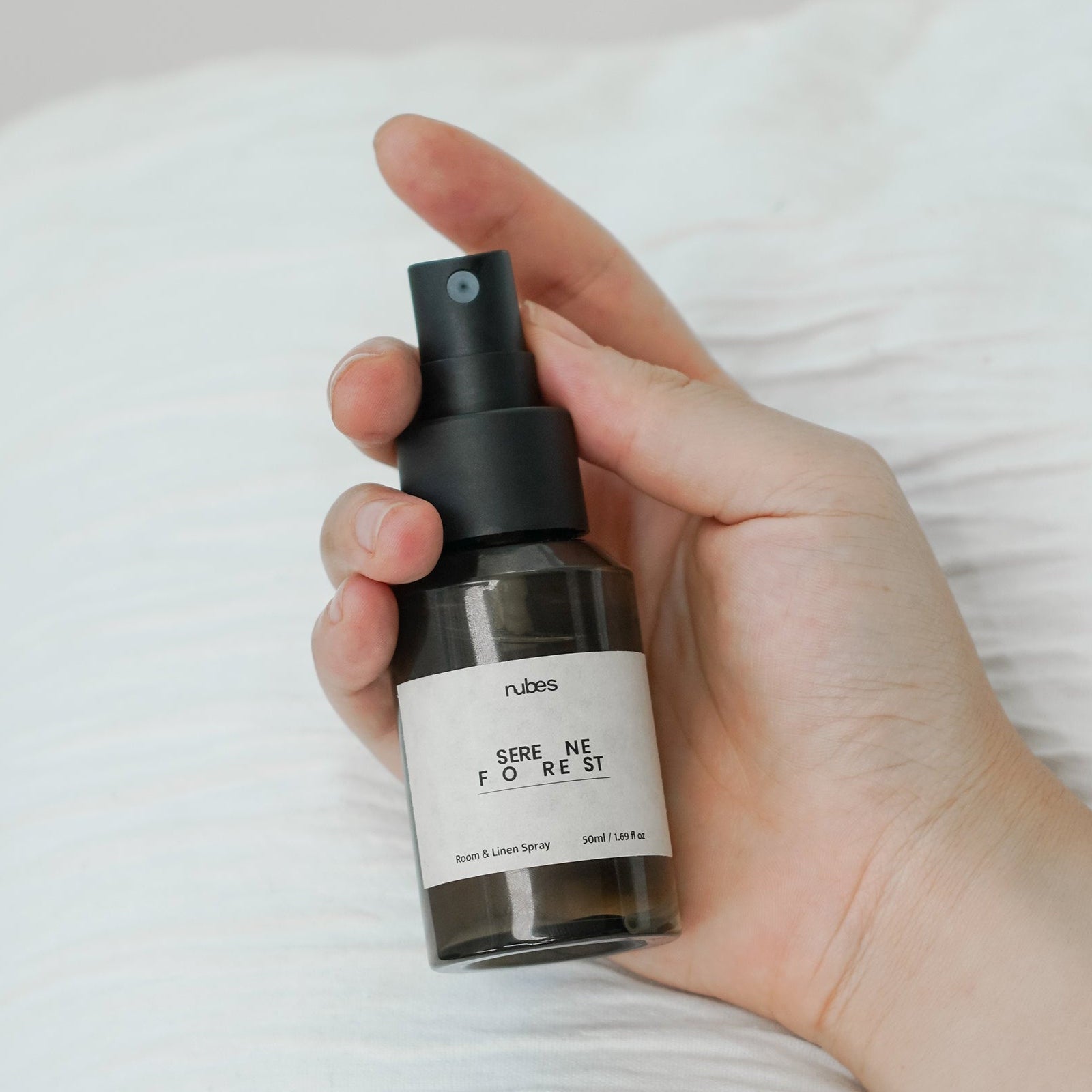 Hand holding a black spray bottle labeled 'nubris' with a white label against a neutral background