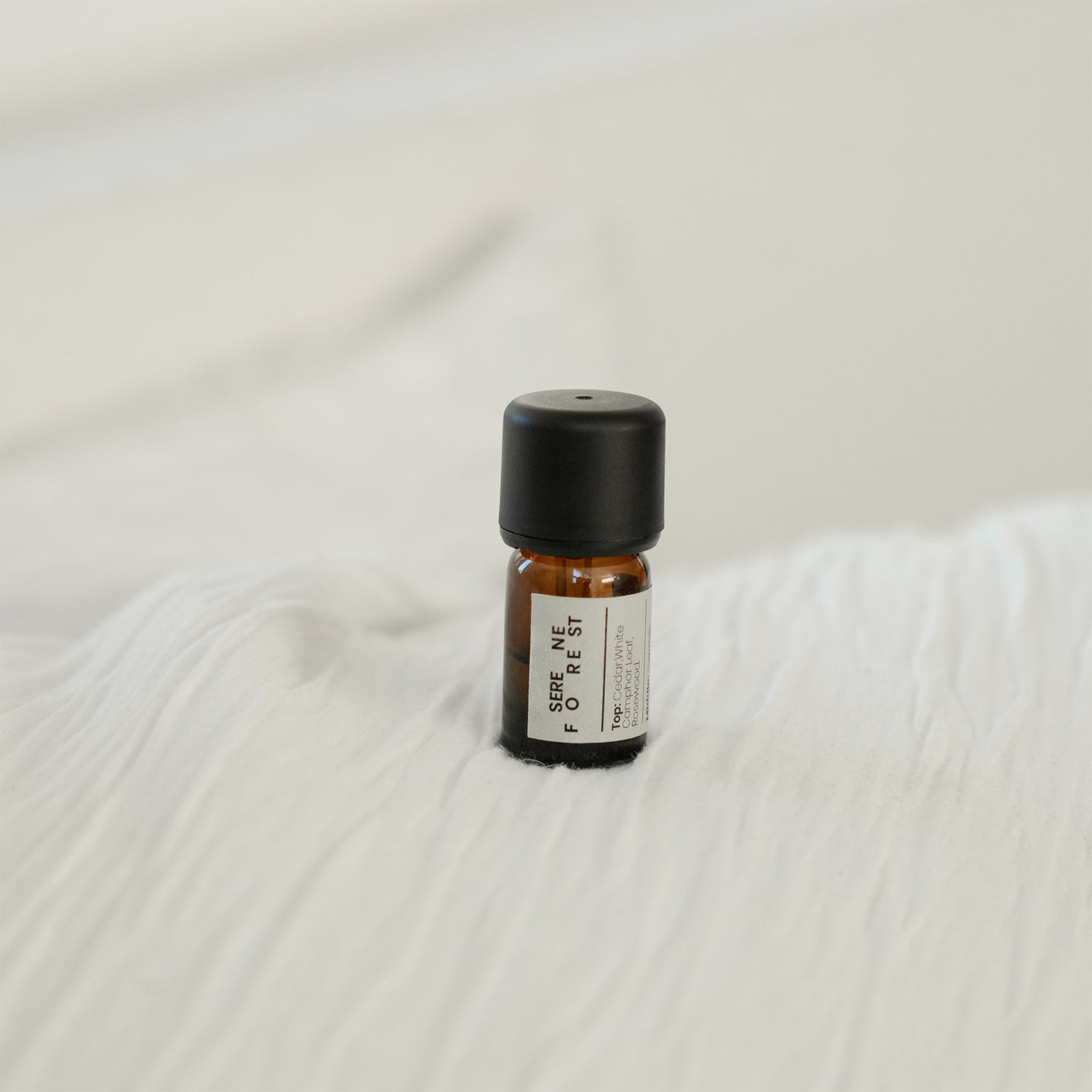 Small essential oil bottle with a black cap on a textured white surface
