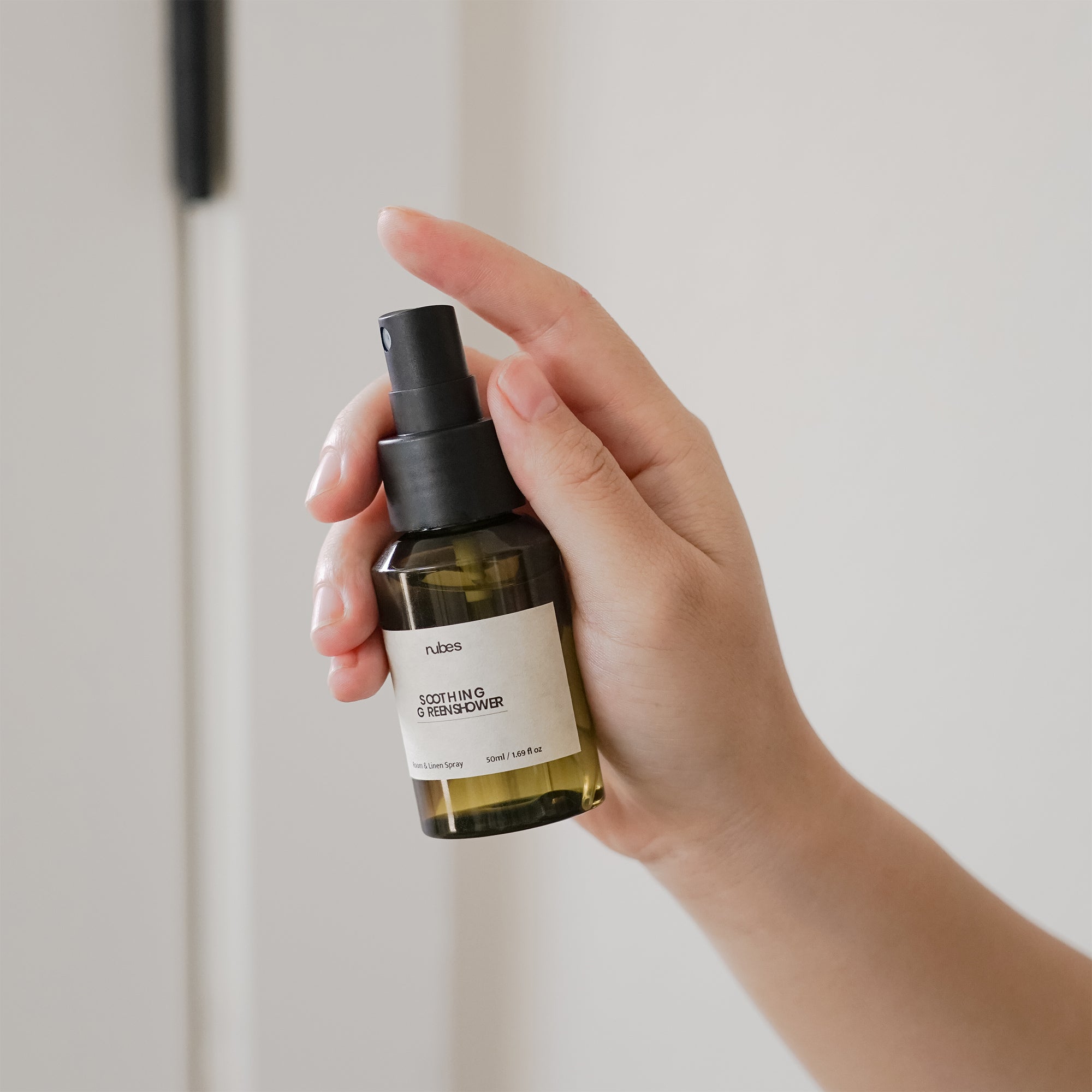 Hand holding a bottle of 'nubes' skincare product against a neutral background